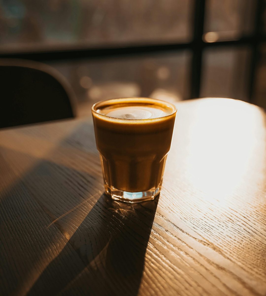 A cozy cappuccino glows in the warm sunset light on a wooden table, inviting relaxation.